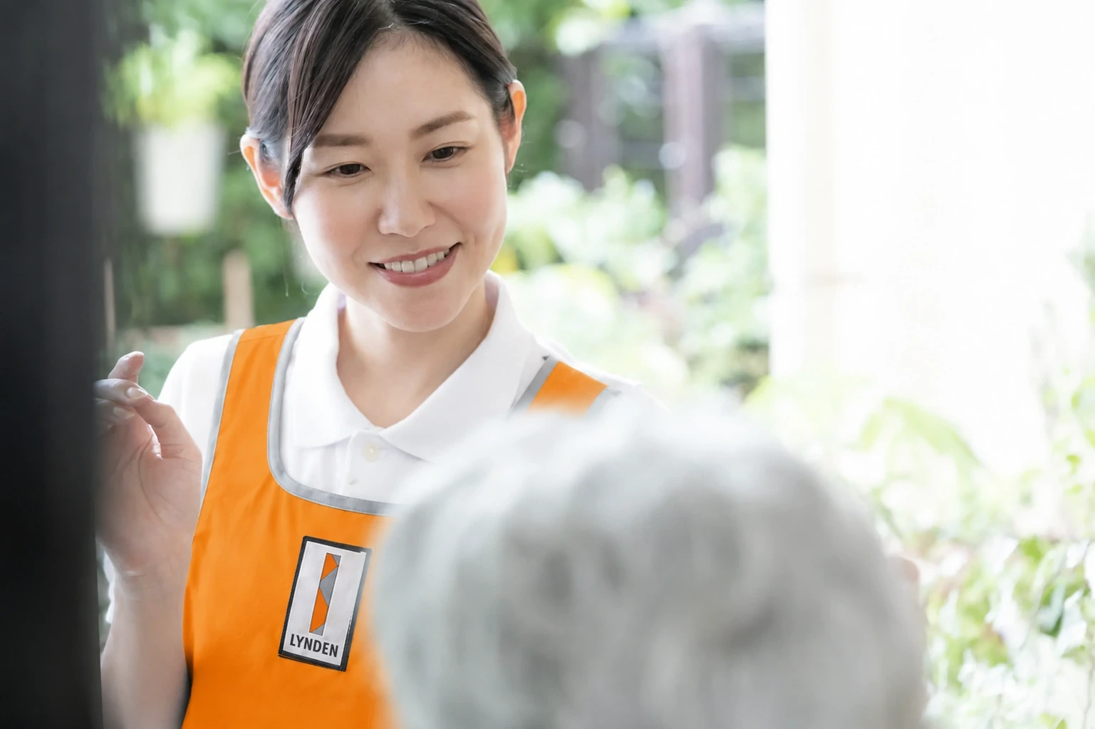 利用者のそばで笑顔で対応するオレンジ色の制服のスタッフ
