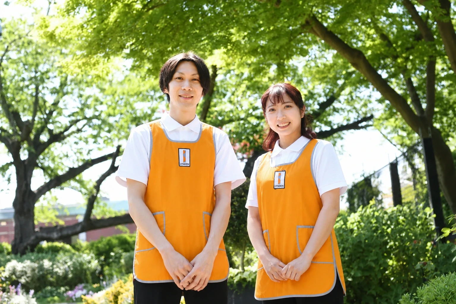 オレンジ色の制服でパソコンの前に座り、ペンを手に笑顔を見せるスタッフ